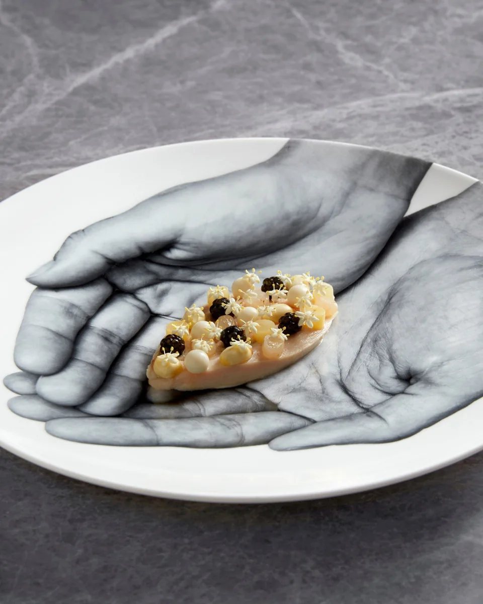Akuna fine dining dish: delicate seafood preparation on an artistic plate with black-and-white hands motif