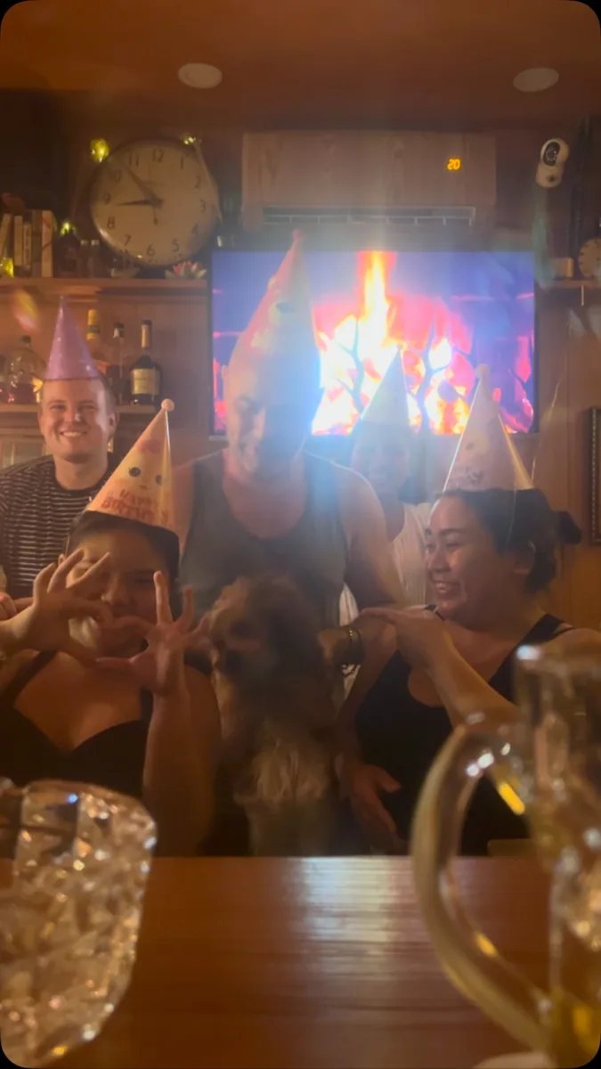 Birthday celebration at Trailer Trash Tavern with patrons in party hats at the bar, fireplace on TV in background